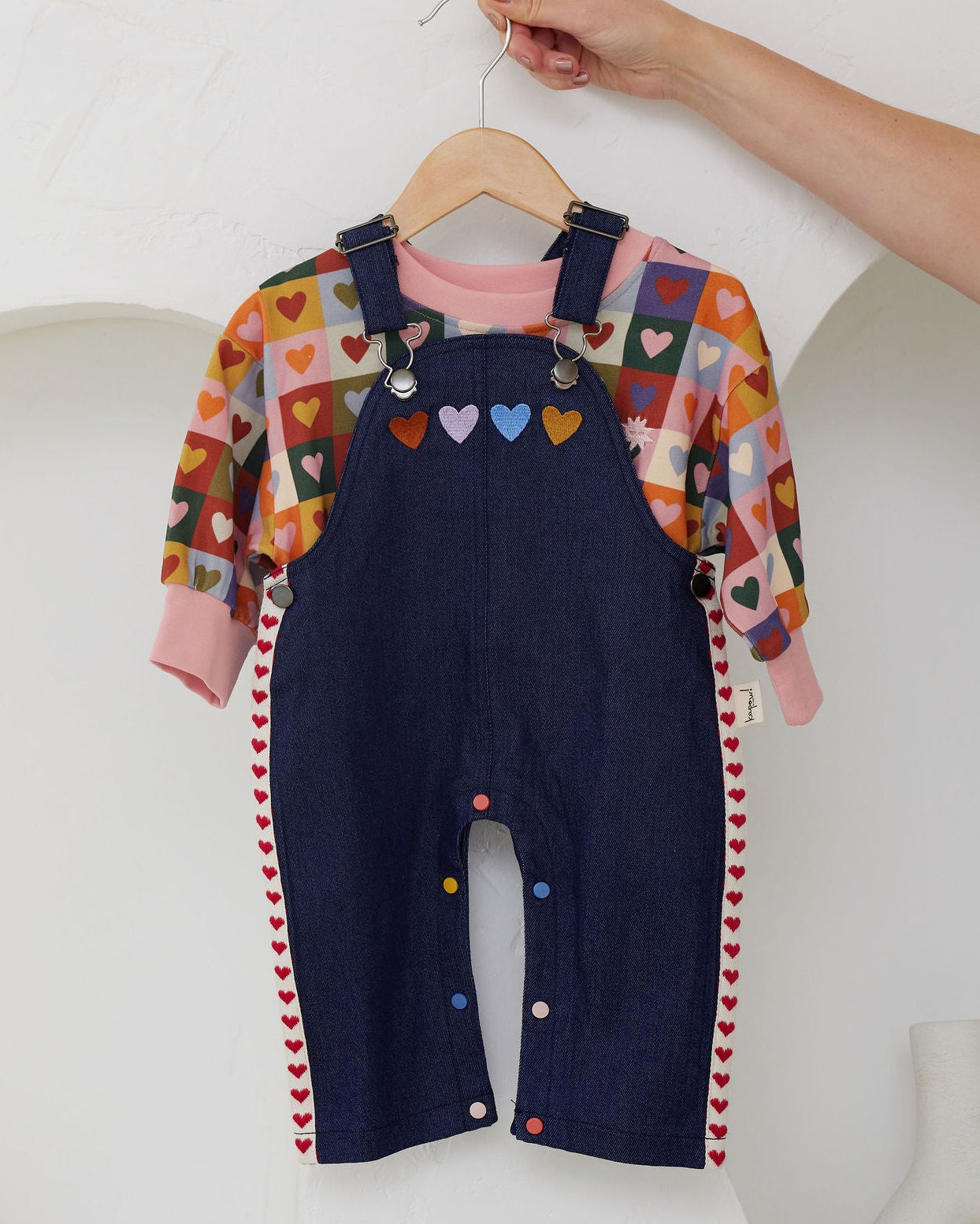 Navy blue overalls with colorful heart-patterned shirt on a hanger against a white background